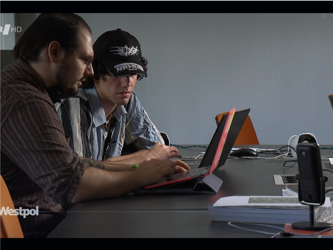 Two men working intently at a laptop in a documentary-style setting