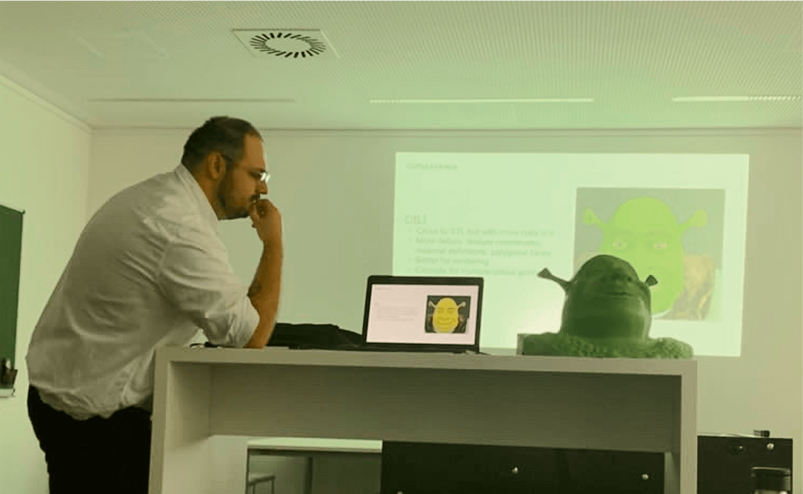 Photo of Denis Malinko leaning over lectern with Shrek bust and projected slide