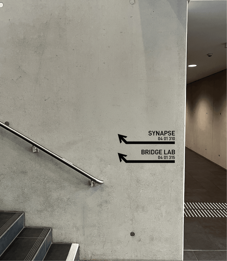 Concrete wall signage pointing left to Synapse and Bridge Lab