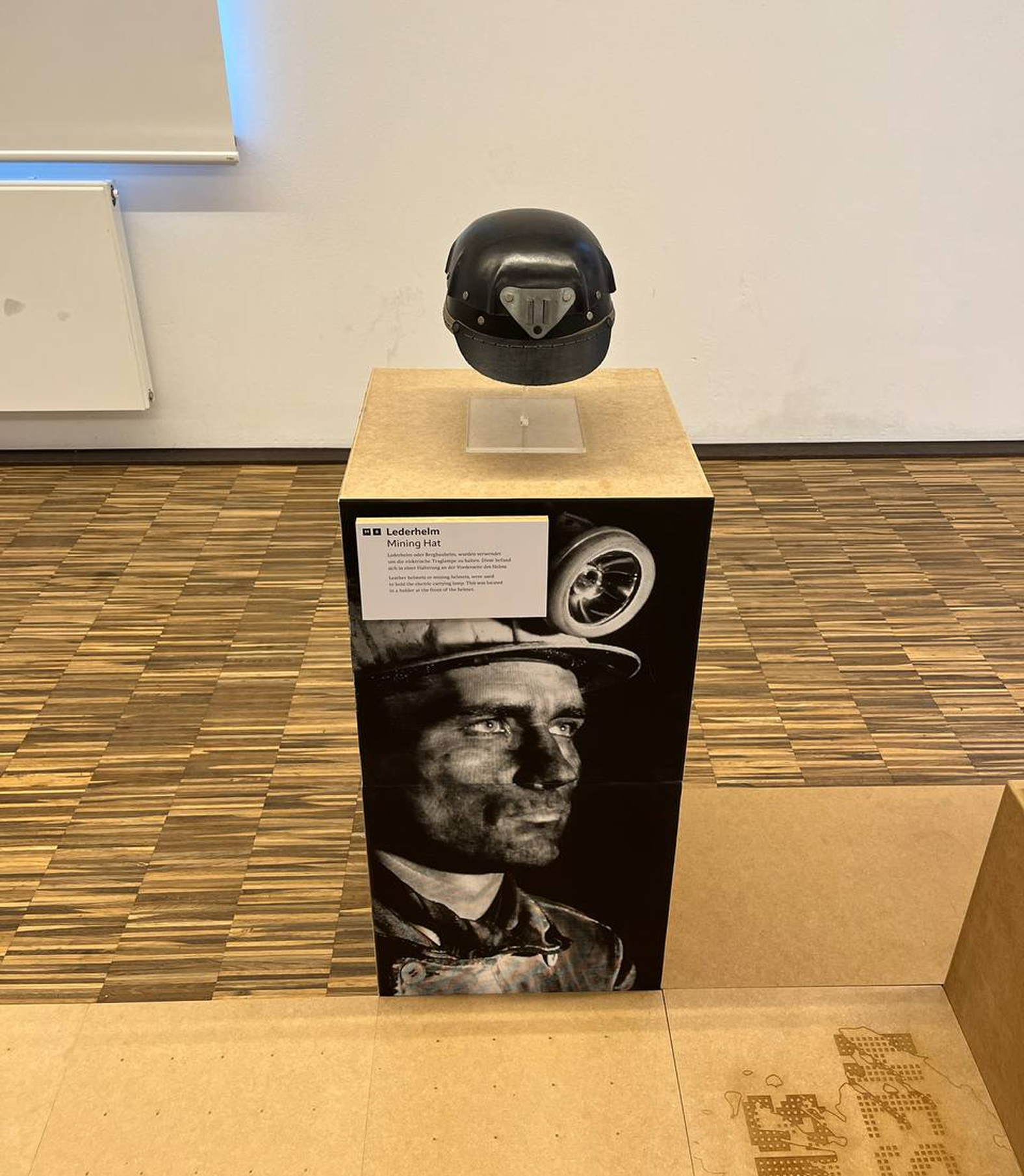 Exhibition pedestal with miner’s helmet and portrait of a coal worker