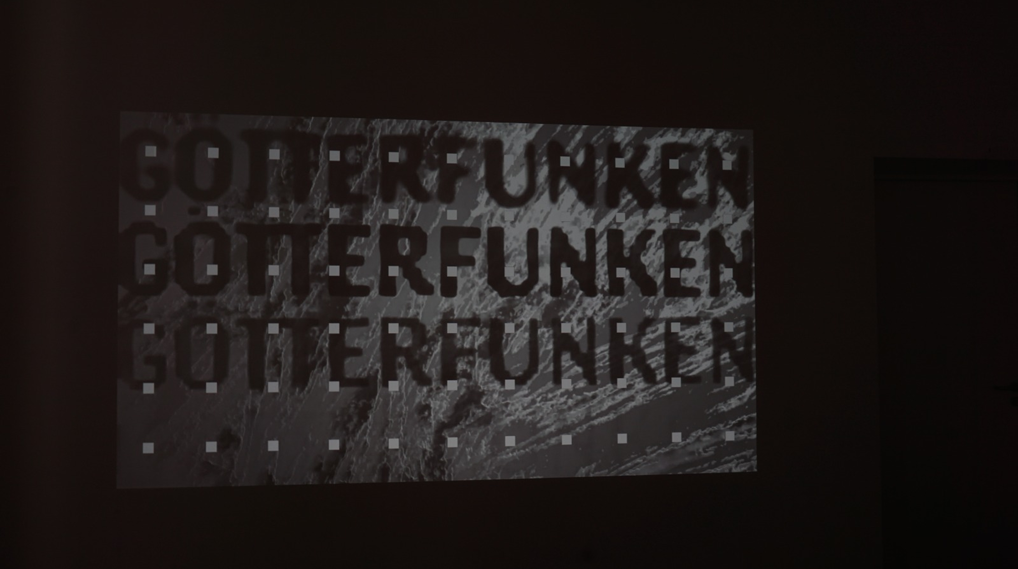 Projected GÖTTERFUNKEN title with pixelated typography on a dark wall