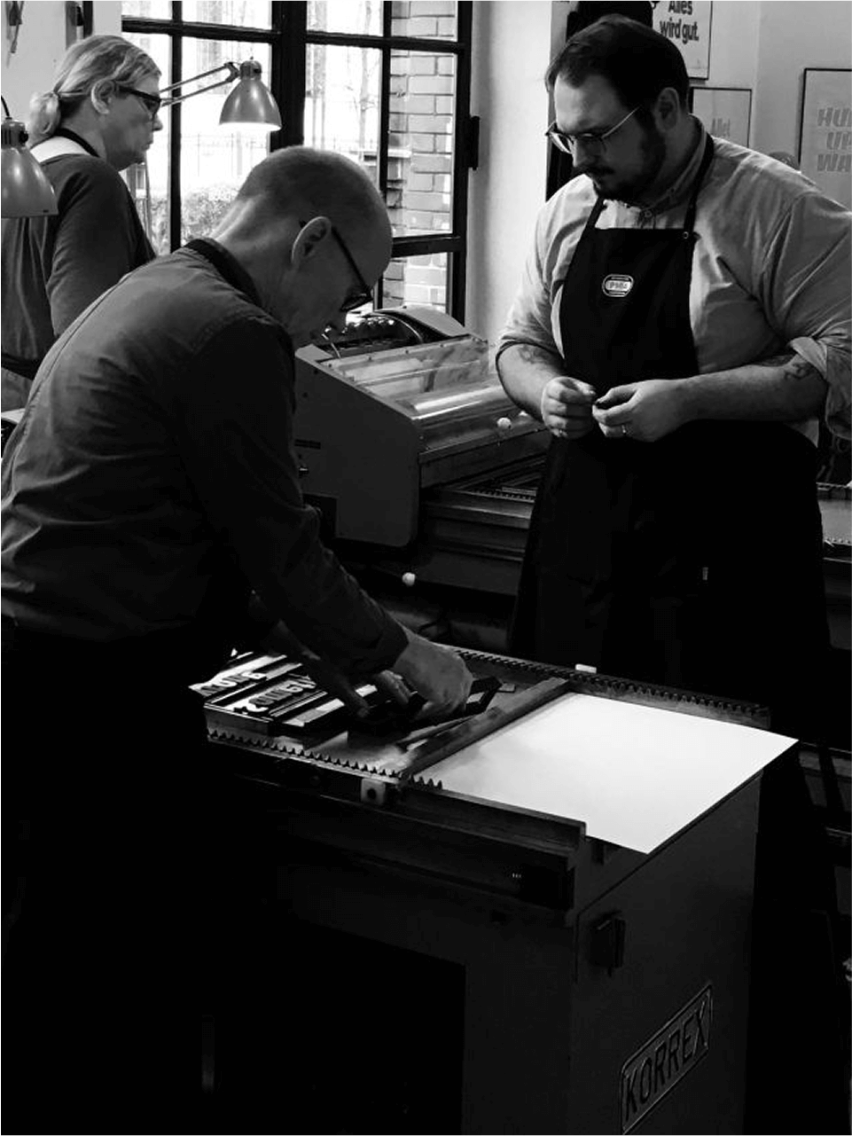Three people, including Denis Malinko, working in a print studio with posters and letterpress equipment