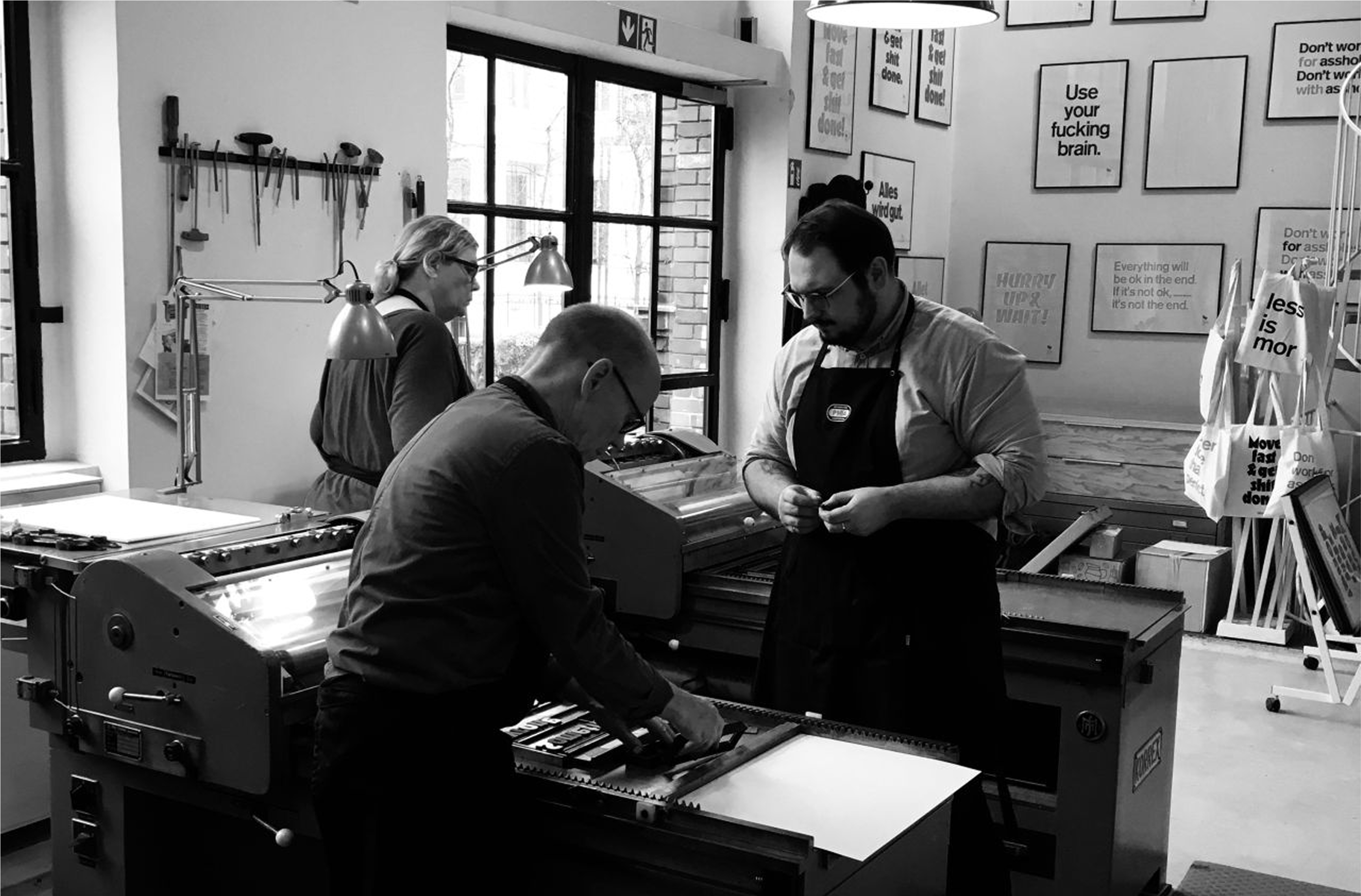 Three people, including Denis Malinko, working in a print studio with posters and letterpress equipment